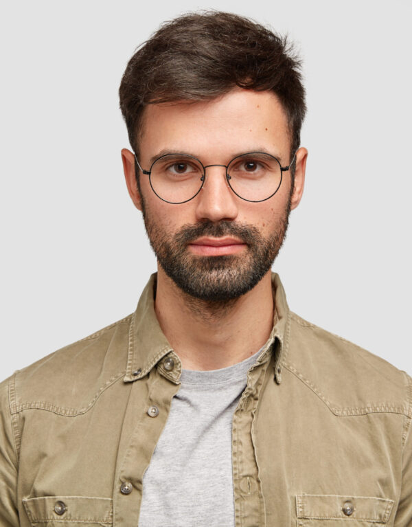 Horizontal shot of handsome unshaven European male has serious self confident expression, wears glasses, looks directly at camera, reads information, isolated over white background. Bearded guy indoor